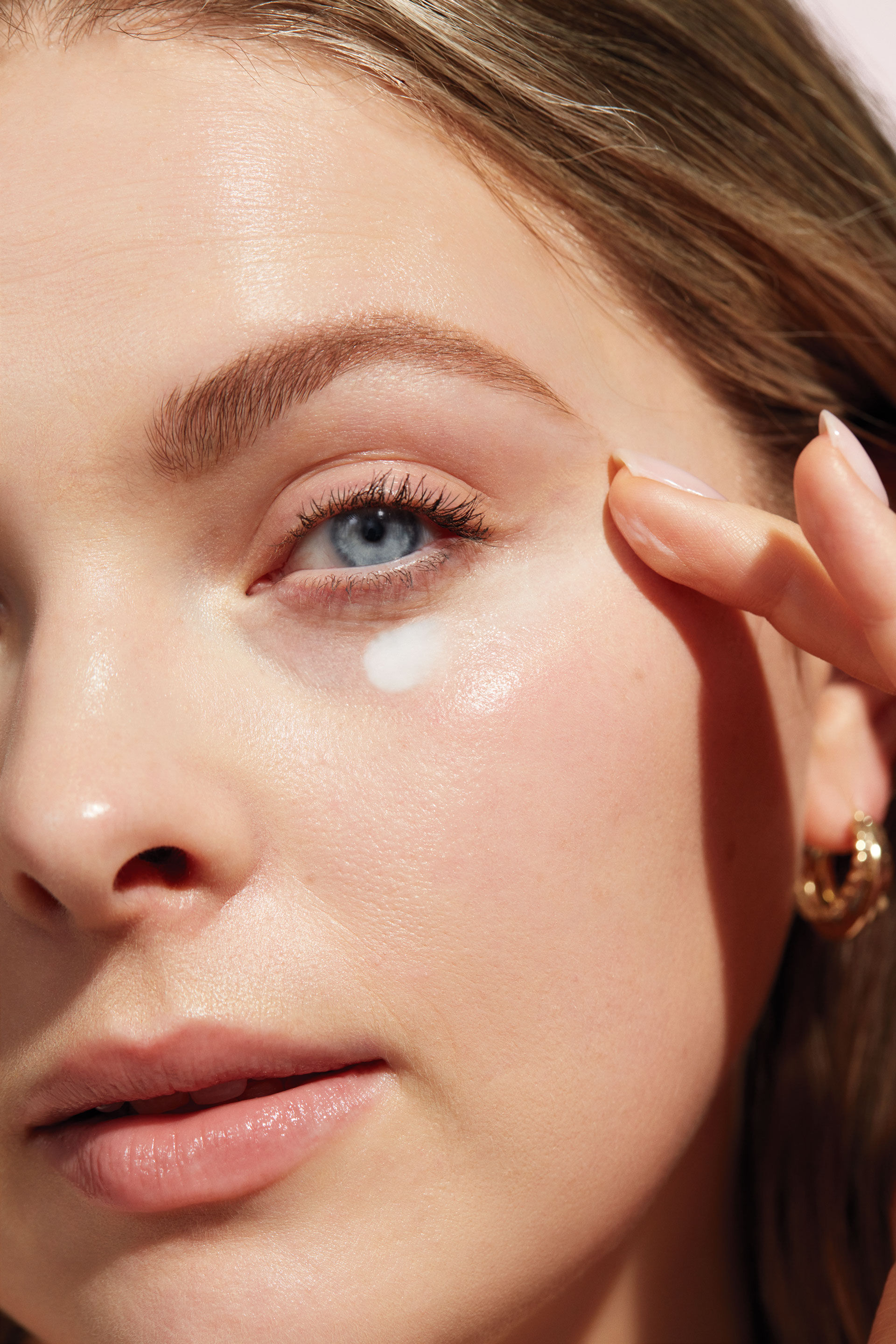 Acercamiento al rostro de una mujer aplic&aacute;ndose crema para ojos Mary Kay con sus dedos.