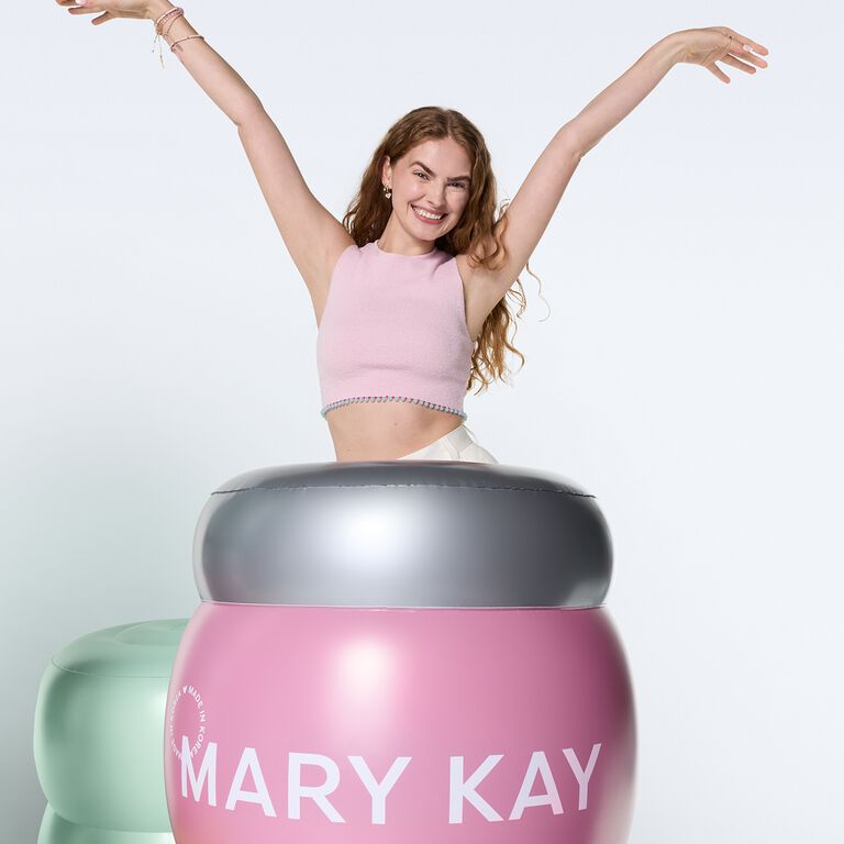 Mujer posando y sonriendo a lado de un inflable de Gel Humectante con Col&aacute;geno Mary Kay&reg; de Edici&oacute;n Especial