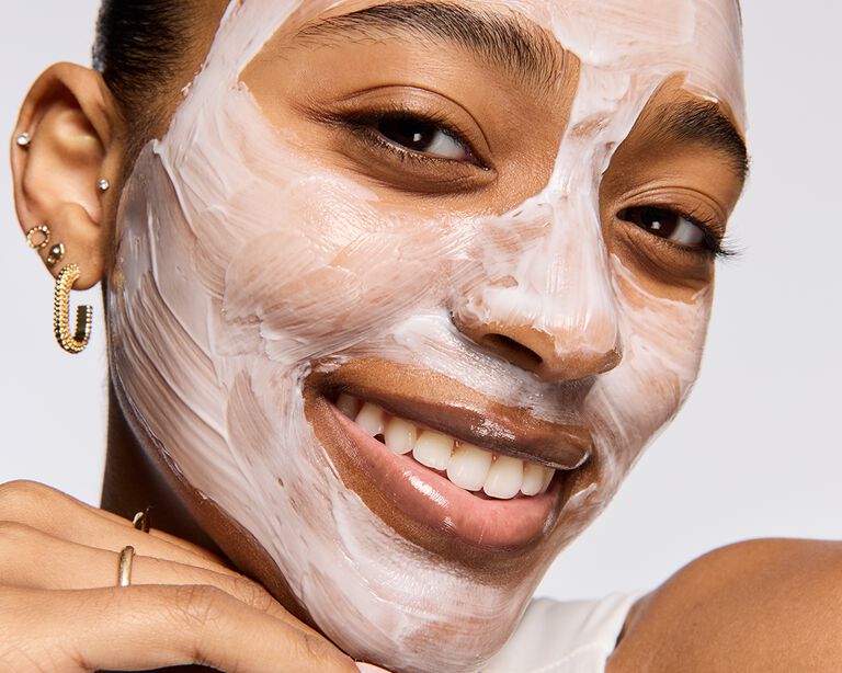 Modelo sonriendo con capa gruesa de mascarilla hidratante.