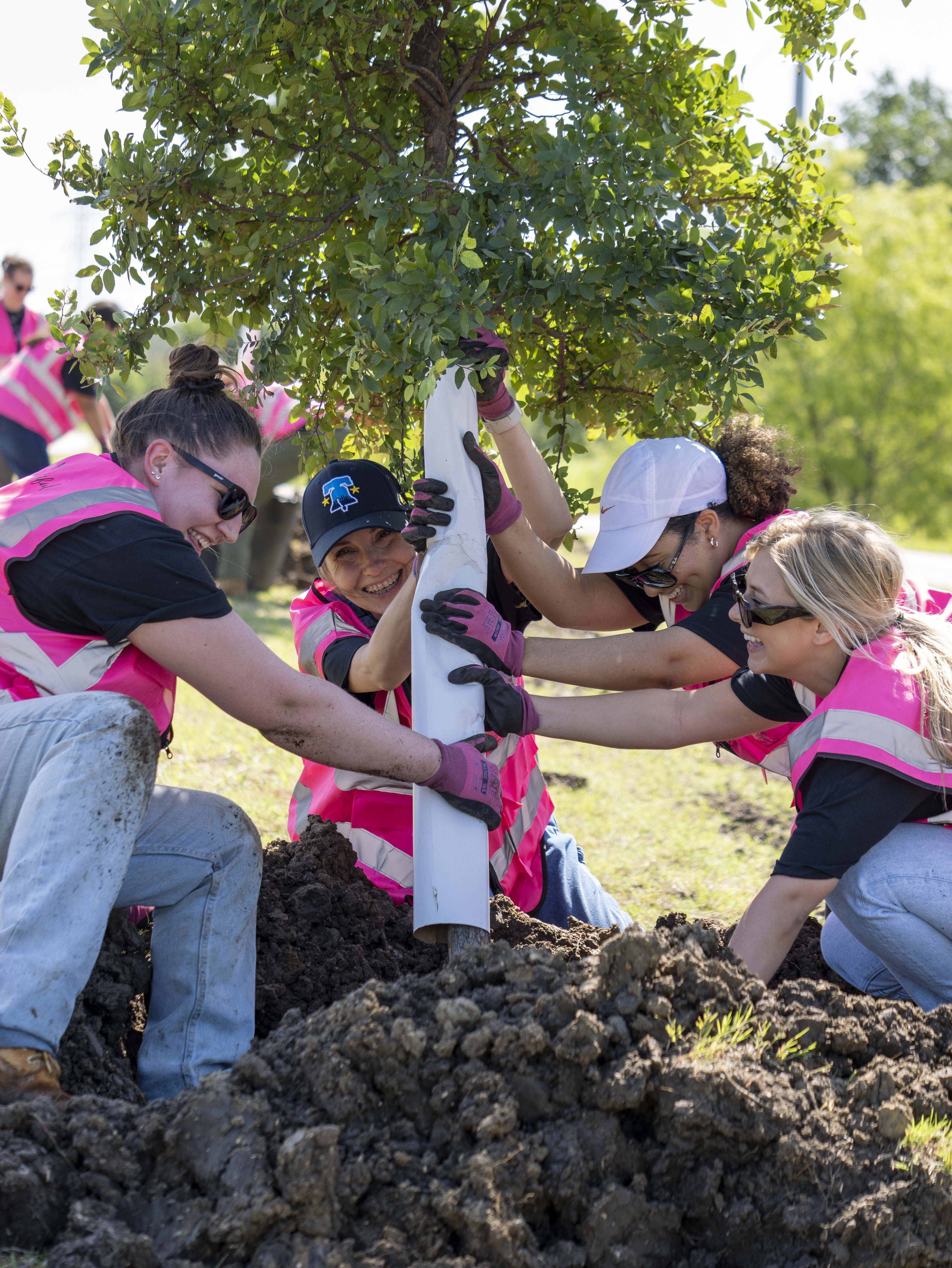 Integrantes de Mary kay vestidos de rosa trabajando juntos plantando un &aacute;rbol.