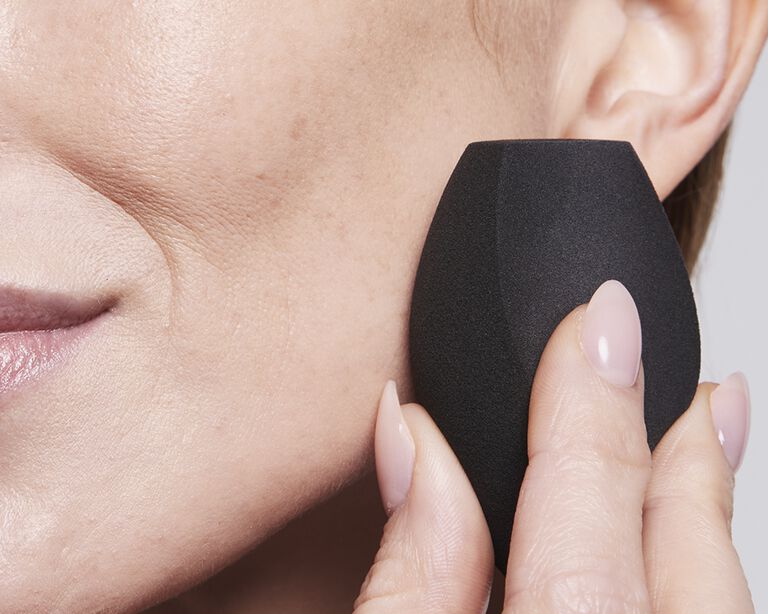 Mujer sosteniendo la Esponja para Maquillaje Mary Kay&reg; en su mejilla, volteando hacia a izquierda y mirando hacia la c&aacute;mara.