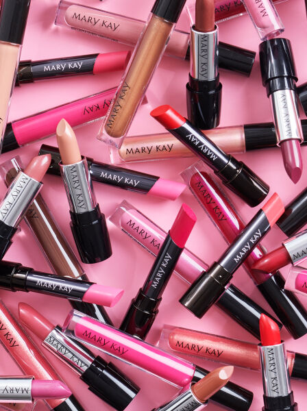 Variedad de labiales y brillos labiales Mary Kay sobre un fondo rosa