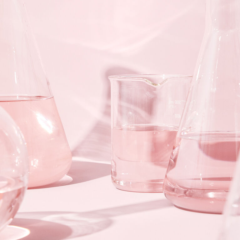 Vasos de precipitados de vidrio cient&iacute;fico sobre un fondo rosa.