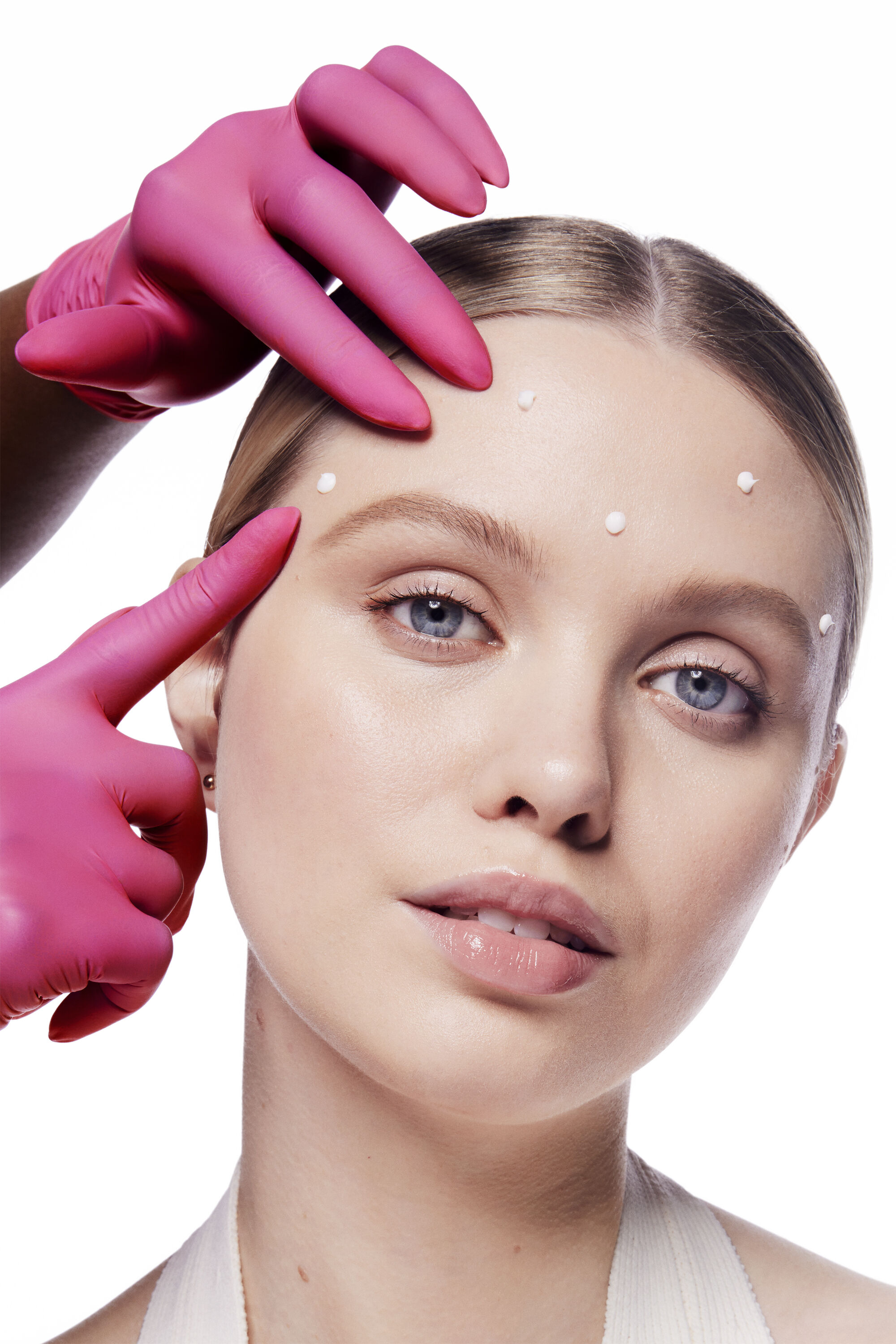Mujer con puntos de Crema Facial con Efecto Tensor de L&iacute;neas de Expresi&oacute;n Din&aacute;micas Mary Kay Clinical Solutions&reg; en la frente. Una mano con guantes rosas toca su frente para dar un efecto cient&iacute;fico.