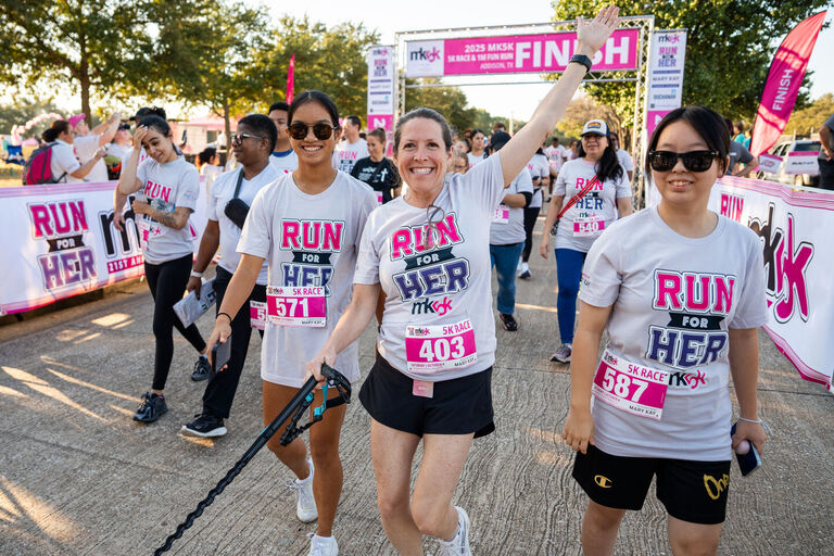 Participantes cruzando la meta en una carrera ben&eacute;fica de 5K, usando playeras de Run for Her