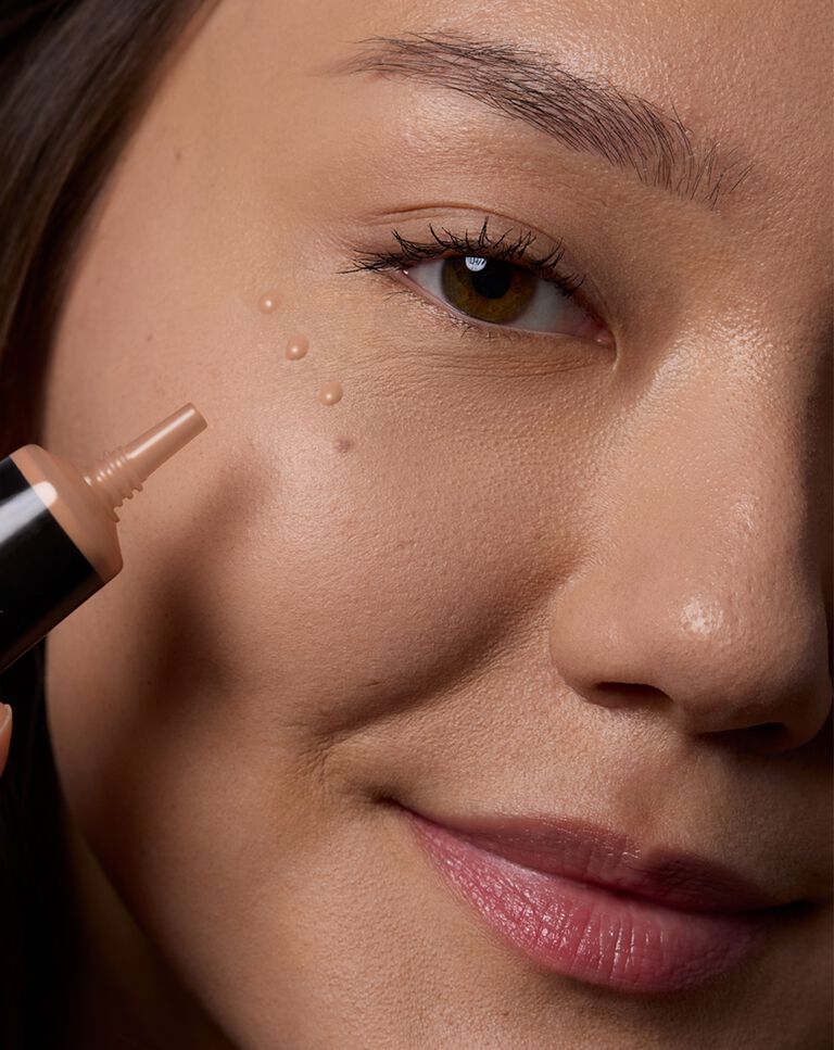 Close-up of a model applying undereye corrector with a makeup sponge