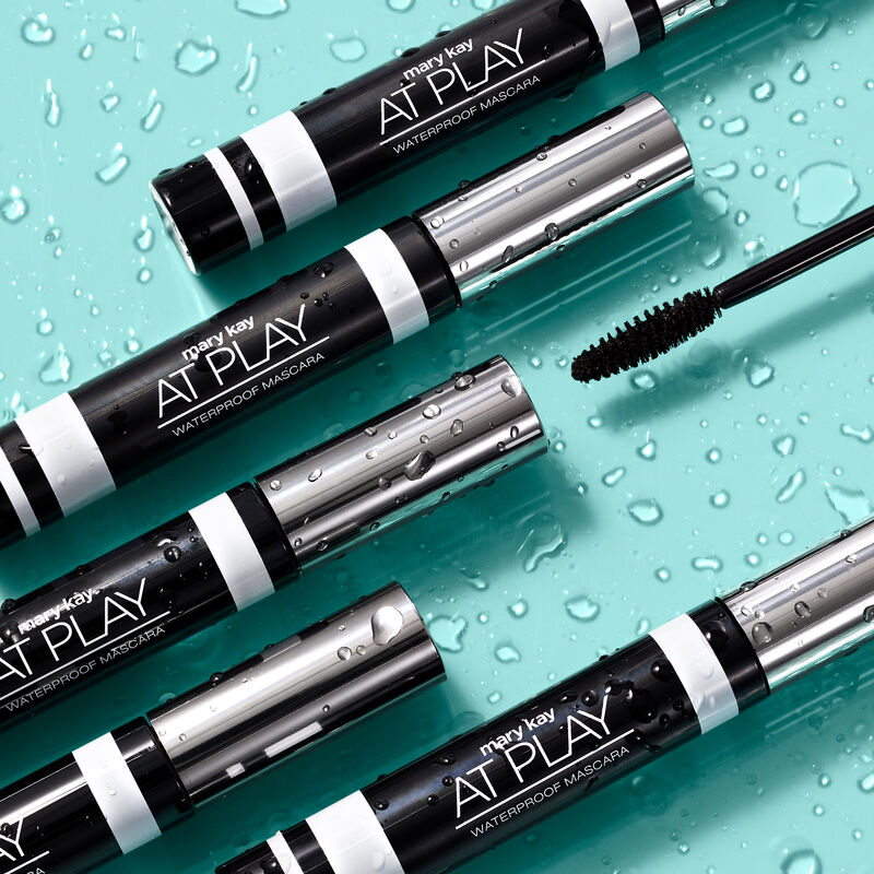 Five tubes of Mary Kay At Play Waterproof Mascara and accompanying wand surrounded by water droplets