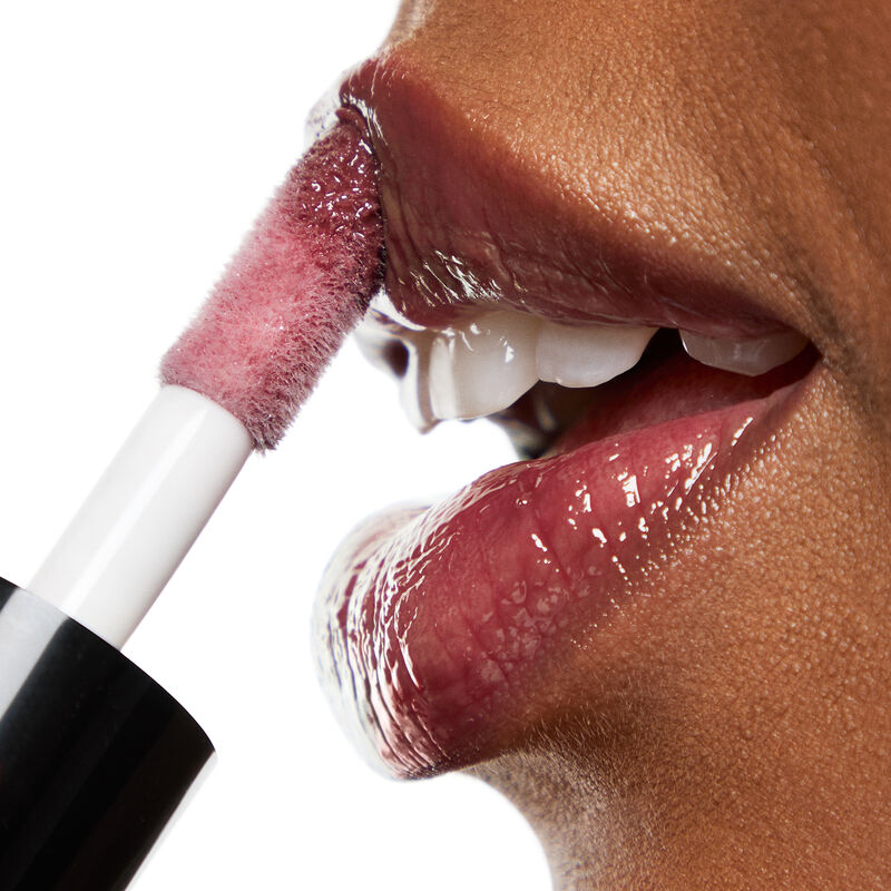 Thick doe foot applicator of Mary Kay Tinted Lip Oil in Berry being applied to lips on deep skintoned woman with a white backgroundnbsp