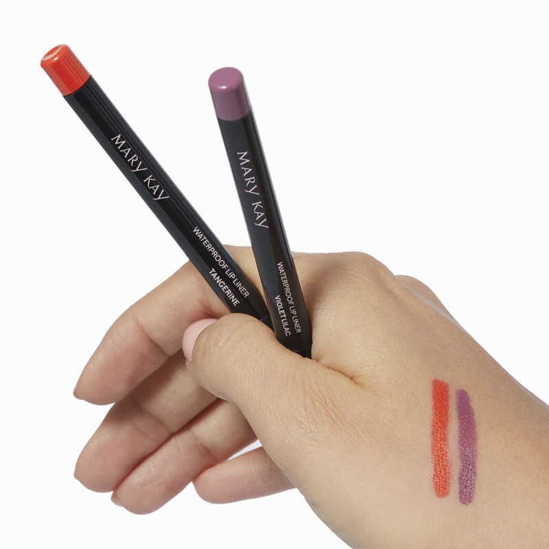 Medium-skinned hand holding special-edition Mary Kay Waterproof Lip Liner pencils in shades Tangerine and Violet Lilac with accompanying product rubs 