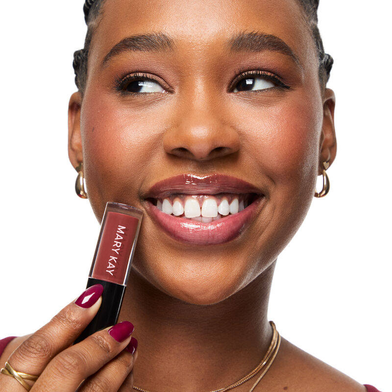 Capped Mary Kay Tinted Lip Oil in Berry held by deep skintoned woman with casually cheerful expression while wearing Berry lip color