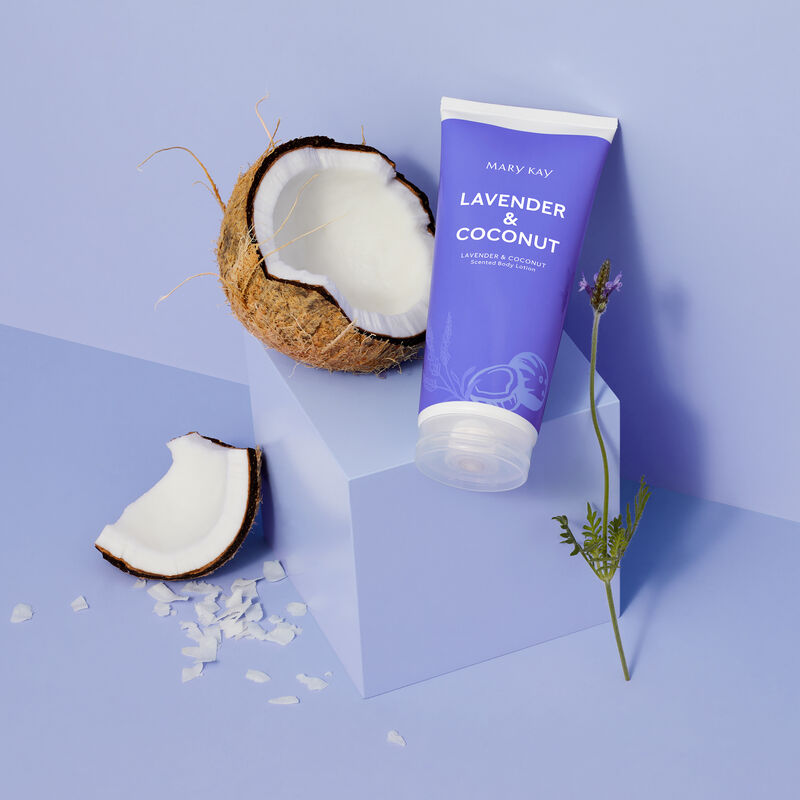 Bottle of limited-edition Lavender & Coconut Mary Kay Body Lotion next to coconut, coconut shavings and lavender stem against light purple background