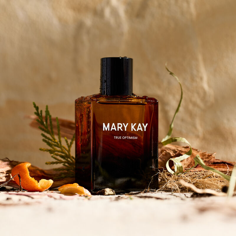 Mary Kay True Optimism Eau de Parfum surrounded by fragrance note ingredients against stone background
