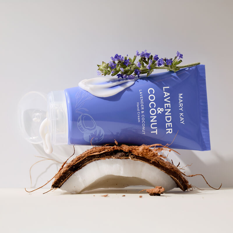 Purple hand cream tube open with product gently squeezed out, balancing on a slice of coconut and sprig of lavender.&nbsp;