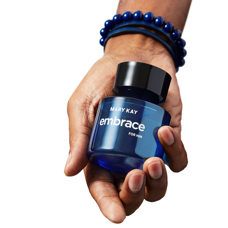 A bottle of Mary Kay Embrace for Him Eau de Toilette being held in the hand of a man with a medium skin tone wearing a beaded bracelet