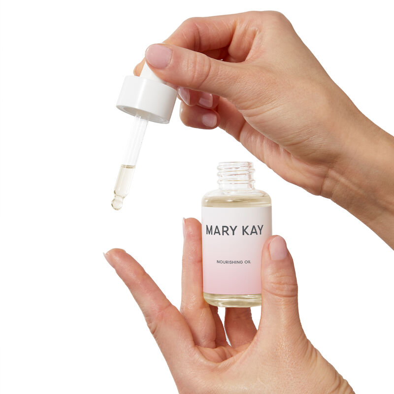 Fair-skinned hands holding bottle of Mary Kay Nourishing Oil and dispensing it with included dropper&nbsp;