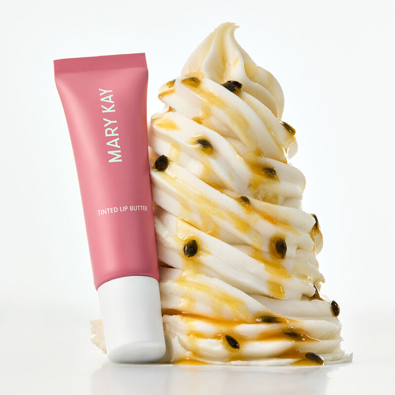 Tinted Lip Butter in Passionfruit Kiss styled against whipped cream with syrup and seeds