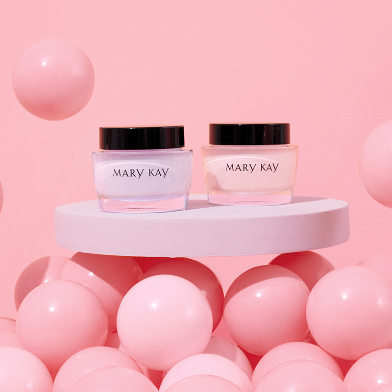 Frascos de Gel Facial Hidratante Libre de Aceite Mary Kay&reg;    y Crema de Extra Hidrataci&oacute;n Intensiva Mary Kay&reg;    colocados sobre una mesa blanca, rodeados de globos rosas. 