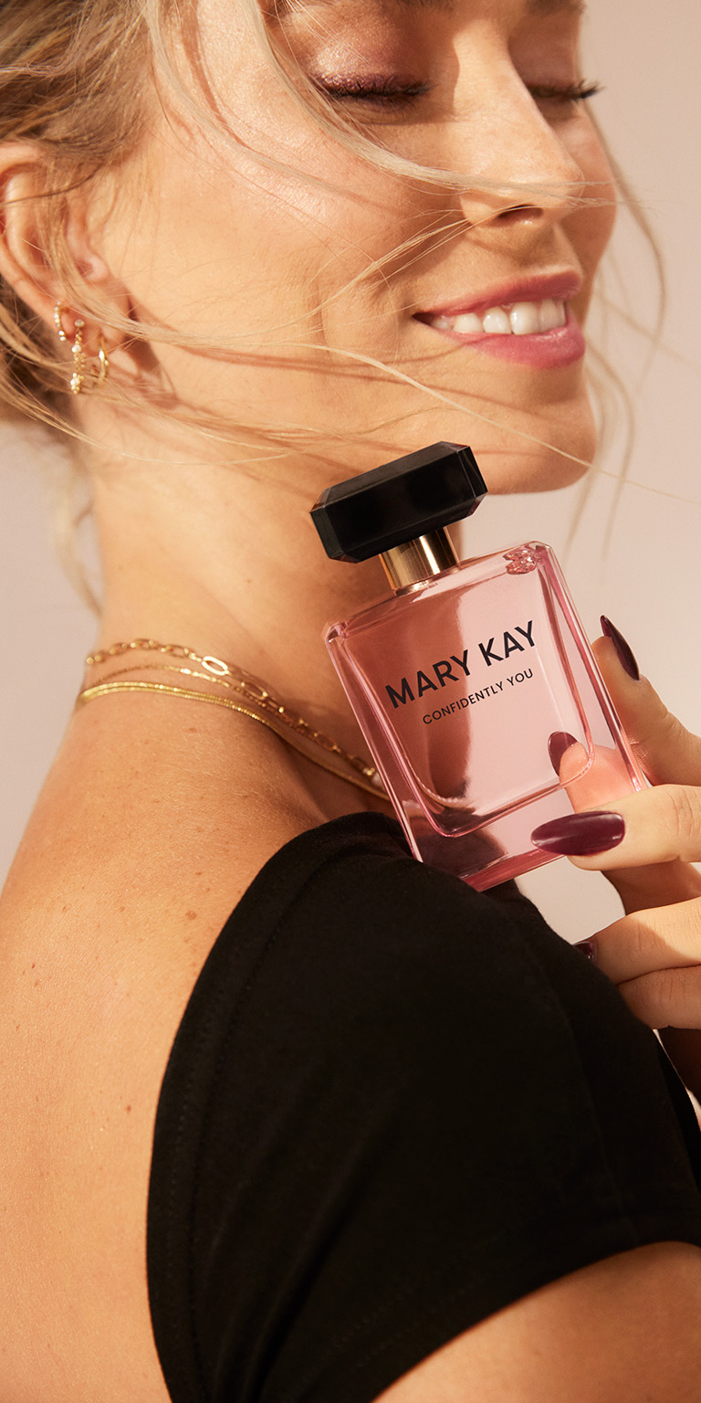 Mujer sosteniendo un frasco de Mary Kay Confidently You Eau de Parfum cerca de su hombro, con un estilo elegante.