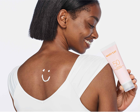 Modelo sosteniendo un tubo de Protector Solar FPS 50+ Mary Kay&reg;, con una carita sonriente dibujada con protector solar en la parte superior de la espalda.