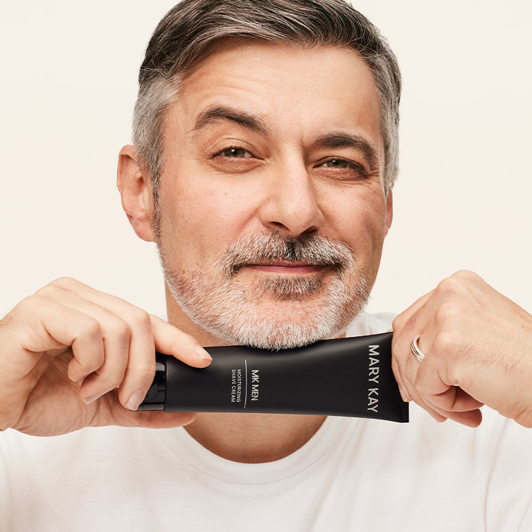 Hombre sonriendo y sosteniendo un tubo de la Crema de Afeitar 2 en 1 MK Men&reg; cerca del ment&oacute;n.