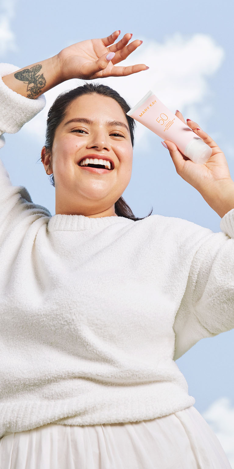 Modelo sosteniendo el Protector Solar FPS 50+ Mary Kay&reg; bajo un cielo azul.
