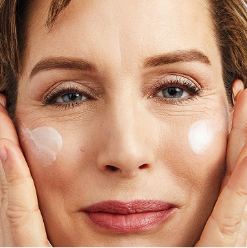 Mujer sonriendo mientras aplica Loci&oacute;n Facial Regeneradora C+E TimeWise&reg; en ambas mejillas.