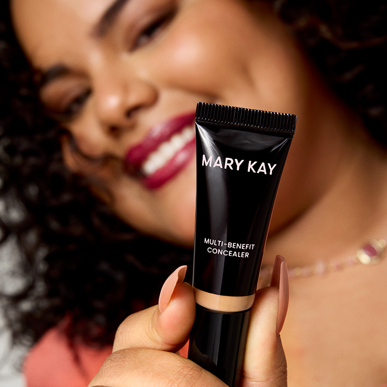 Mujer sonriendo y mostrando el Corrector para Ojos Multi‑Beneficios Mary Kay&reg; hacia la c&aacute;mara
